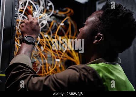 Close up of black man as network technician connecting cables and wires while repairing server in data center Stock Photo