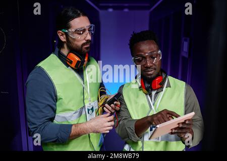 Waist up portrait of two network technicians using tablet while repairing server in neon light Stock Photo