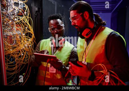Close up of two network technicians using tablet while repairing server in neon light Stock Photo