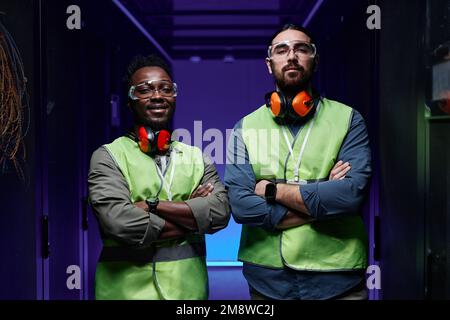 Waist up portrait of two technicians standing in server room with arms crossed and looking at camera lit by neon light Stock Photo