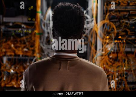 Back view of black young man as system administrator looking at servers, copy space Stock Photo