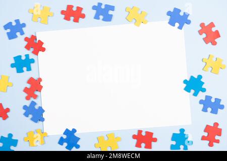 Blank white paper card with blue, yellow, red pieces of puzzle on light blue frame background. World autism awareness day concept. Top view, copy Stock Photo