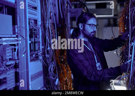 Side view portrait of bearded man as system administrator working with server in neon light, copy space Stock Photo