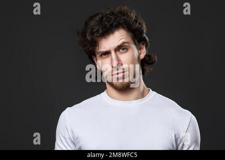 skeptic and nervous man in white t-shirt on dark gray background Stock Photo
