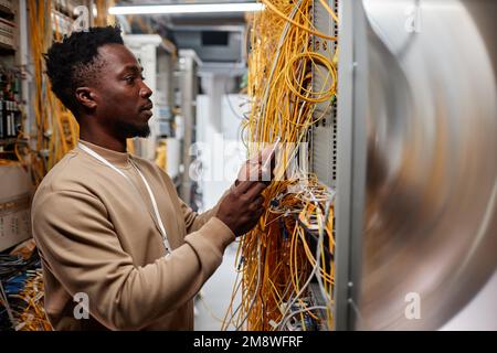 Side view portrait of black man as system administrator setting up server and using smartphone Stock Photo