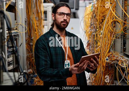 Waist up portrait of bearded man as system administrator standing in server room and looking at camera Stock Photo