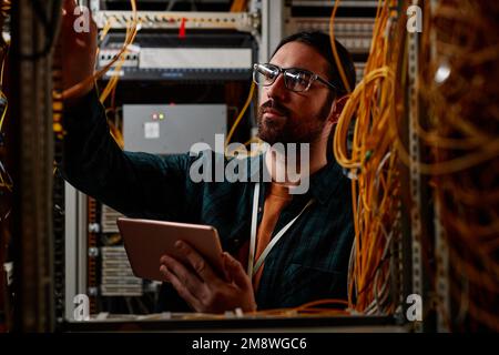 Front view portrait of bearded man setting up server while working with data network and holding tablet Stock Photo