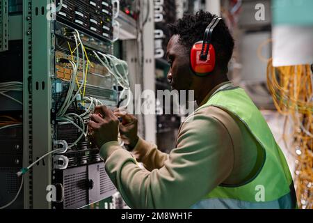 Side view portrait of young technician setting up network in server room and wearing protective workwear Stock Photo