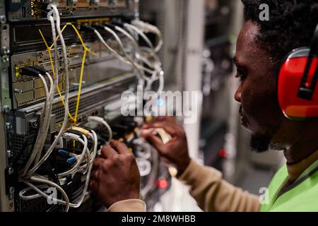 Close up of technician setting up network in server room and wearing ear protection Stock Photo