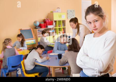 Upset girl in schoolroom on background with pupils Stock Photo