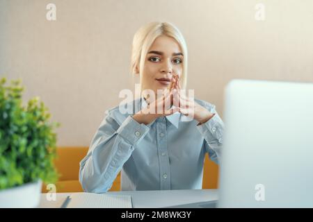 Young beautiful blonde businesswoman or college student works on laptop at home or in office. Online seminar, distance learning or job concept. Stock Photo