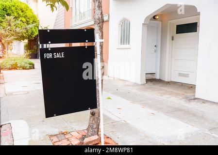 Close up of a real estate sign on the sidewalk in front of a house on sale Stock Photo