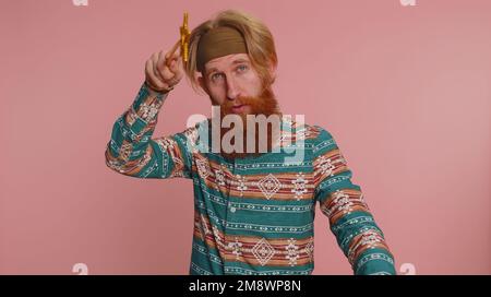 Magician wizard man gesturing with magic wand fairy stick, making wish come true, casting magician spell, advertising holidays sale discount. Young redhead hippie guy isolated on pink wall background Stock Photo