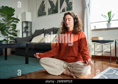 Young mindful woman wearing headphones listening music doing meditation at home. Stock Photo