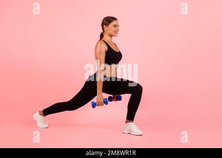 Sporty Young Woman Holding Dumbbells And Making Deep Lunges Exercise In Studio Stock Photo