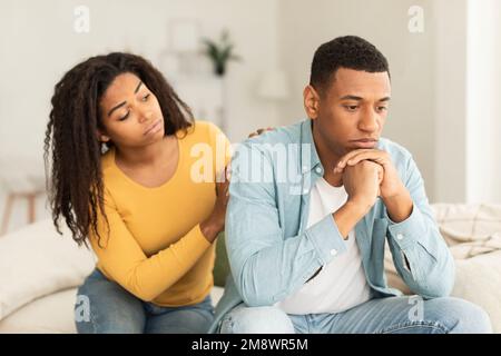 Serious young african american female calms offended sad male sit on sofa in room interior Stock Photo