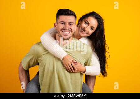 Smiling handsome millennial strong arab guy hold lady on back, have fun together Stock Photo