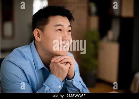 Dreamy middle aged asian businessman thinking of new business strategy, looking aside and smiling, free space Stock Photo