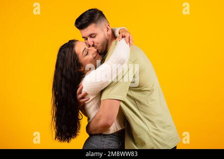 Satisfied handsome millennial middle eastern man hugging and kissing female, couple enjoy free time Stock Photo