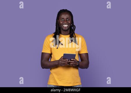 Happy stylish young black guy using digital pad on purple Stock Photo