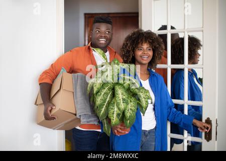 Excited black couple entering their apartment and carrying boxes with belongings