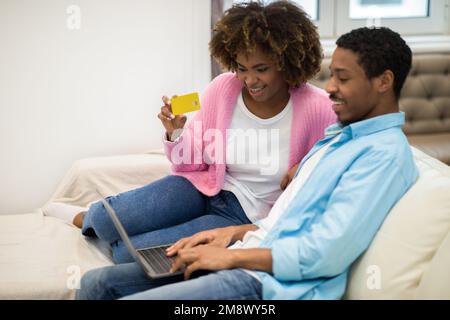 Happy black spouses banking from home, using laptop, credit card Stock Photo