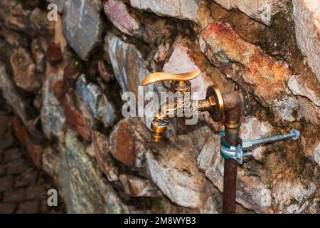 Antique brass water faucet as an architectural monument. Old tap with water on the street. Stock Photo