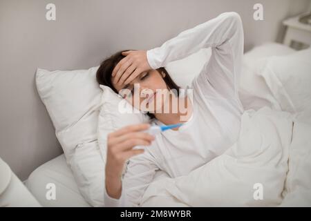 Sick woman with fever checking her temperature in bed Stock Photo