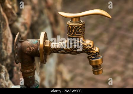 Antique brass water faucet as an architectural monument. Old tap with water on the street. Stock Photo