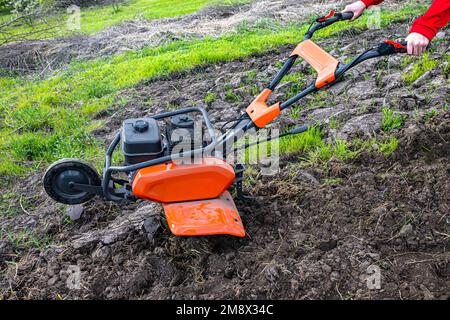 Motor cultivator with a raised front wheel and a furrow inserted into the ground during ploughing of the field before sowing seeds and planting seedli Stock Photo