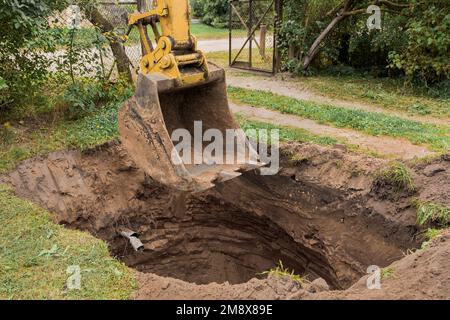 A bucket of excavator over a large deep pit in the ground. Construction or industrial excavation work. Stock Photo