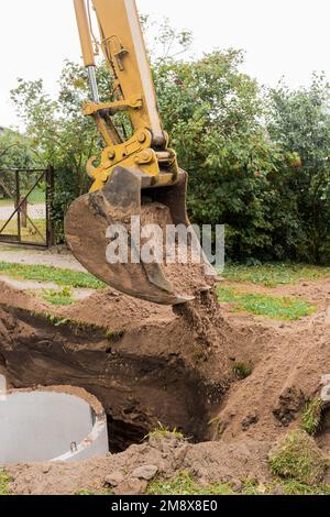 A bucket of excavator with a pile of sand and earth buries sewer concrete rings in the industrial zone. Stock Photo