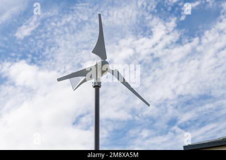 Wind turbine on the roof of a residential house with blue sky and clouds in the background, renewable energy source. Stock Photo
