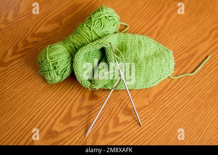 Knitted sock, ball of yarn and circular knitting needles on a wooden table surface. Top view. Stock Photo