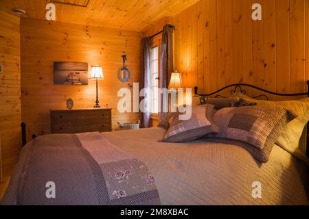 Queen size bed with cast iron headboard and footboard in guest bedroom with wood plank walls on upstairs floor inside milled log home. Stock Photo