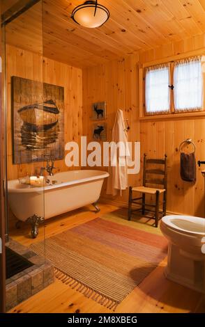 Claw foot bathtub, antique wooden high back chair and toilet in main bathroom on upstairs floor inside milled log home. Stock Photo