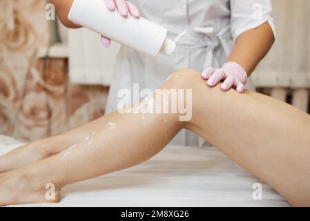 woman's hands of a beautician preparing a slender female legs to the procedure of sugar hair removal in a professional salon. The concept of depilator Stock Photo