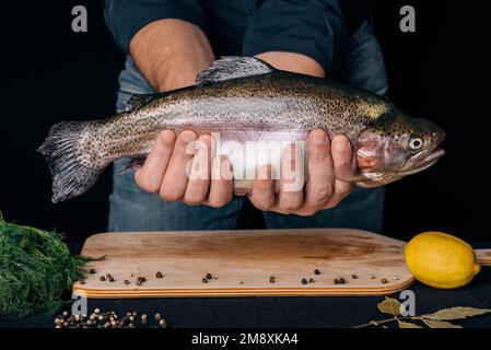 fish in the hands of men on the background of the kitchen with a table with ingredients. Large fresh trout Stock Photo