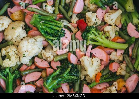 sausages with broccoli, cauliflower and string beans are fried in a frying pan close-up Stock Photo