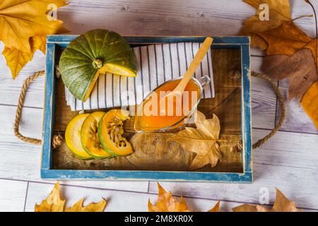 Top view of homemade pumpkin marmalade in a glass jar on a wooden tray with dried leaves Stock Photo