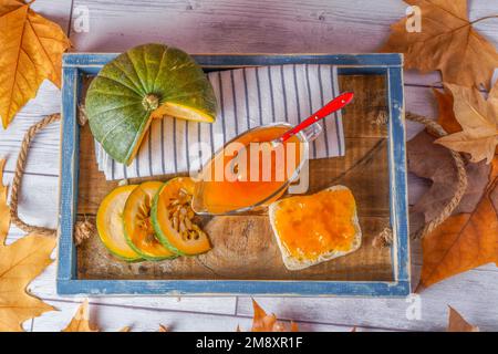 Top view of homemade pumpkin marmalade in a glass jar on a wooden tray with dried leaves Stock Photo