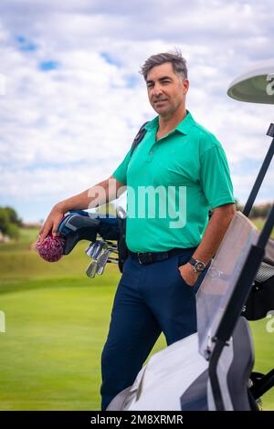 A professional golf player in a green polo shirt with the bag of clubs Stock Photo