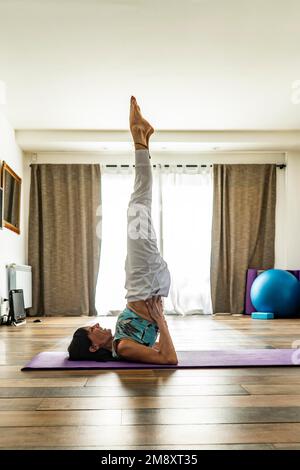 Side view of a woman practicing yoga, doing Shoulderstand pose. Yoga Studio Stock Photo