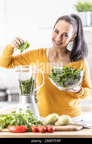 Smiling woman making spinach smoothie, putting leaves in blender. Concept of healthy lifestyle and eating. Stock Photo