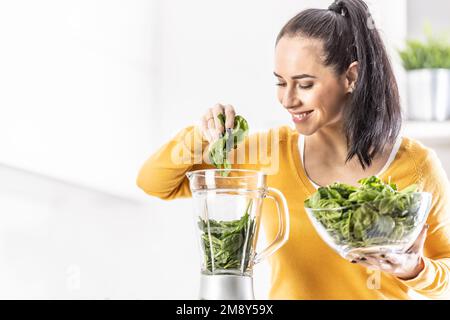 Smiling woman making spinach smoothie, putting leaves in blender. Stock Photo