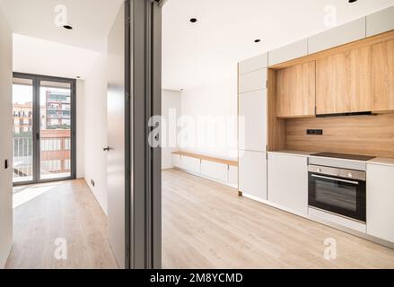 Empty contemporary kitchen, living room and bedroom with balcony at refurbished apartment. Wooden furniture and modern appliances Stock Photo