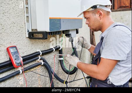 Man electrician installing solar panel system. Inspector in helmet and gloves making electrical wiring inverter and electric box. Concept of alternative and renewable energy. Stock Photo