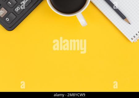 Notepad, calculator, coffee cup and on a yellow background, flat lay. Stock Photo