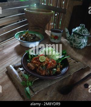 Sambal tempe served with boiled vegetables on a clay plate against a bamboo material background Stock Photo
