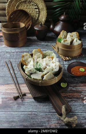 Dumplings of various flavors are served on a bamboo tray with cups and teapots in the background Stock Photo